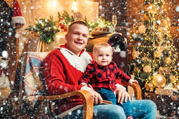 Mutlu baba ve küçük çocuğun portresi ahşap arka planda ve lüks süslemeli odada Noel ağacına karşı sandalyede oturuyor. Aile kış tatili ve insanlar konsepti. — Stok fotoğraf