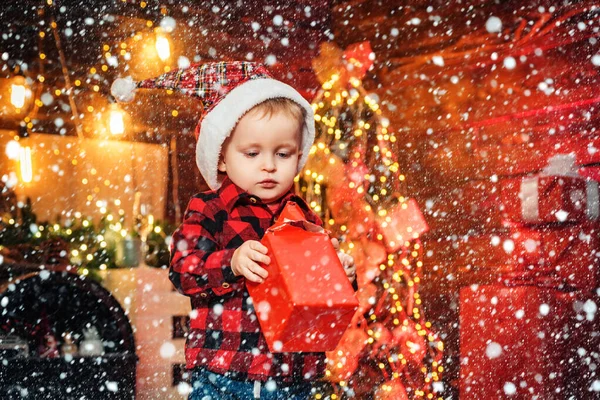 Kleines Baby mit Weihnachtsgeschenk in der Hand auf dem weihnachtlichen Hintergrund. Kleines Kind mit Weihnachtsmütze. Frohe Weihnachten und frohe Feiertage. — Stockfoto