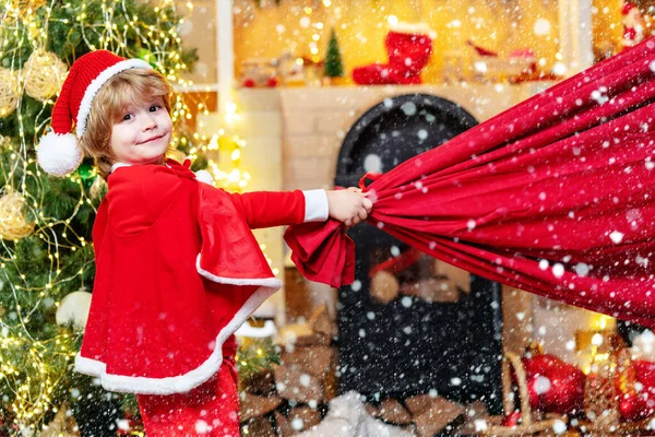 Santa Claus helper carrying big bag full of gifts. Santa helper holding a red bag with presents. Dreamy toddler on Christmas eve. Santa helper.