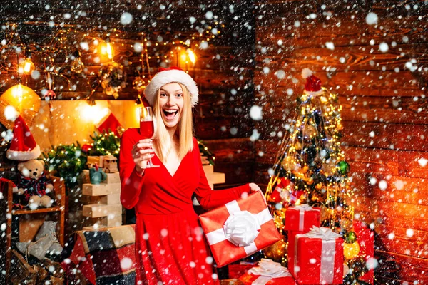 Menina de Natal em vestido vermelho com champanhe. Santa mulher posando no fundo de madeira vintage. Mulher em vestido de noite sobre fundo árvore de Natal em casa. Véspera de Ano Novo celebrando conceito . — Fotografia de Stock