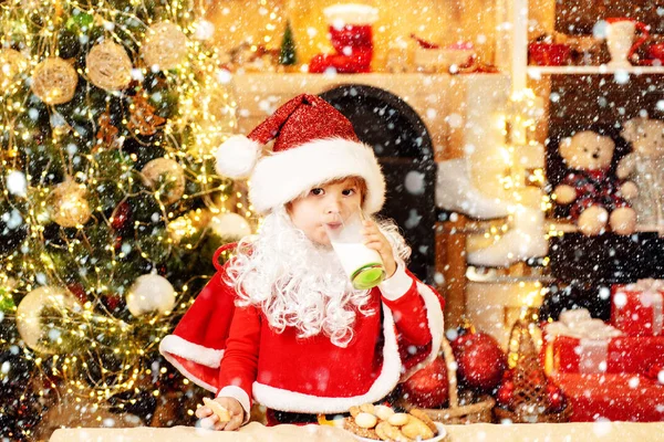Der Weihnachtsmann isst an Heiligabend Plätzchen und trinkt Milch. Der kleine Weihnachtsmann pflückt zu Hause Plätzchen und ein Glas Milch. Frohe Weihnachten und ein gutes neues Jahr. — Stockfoto