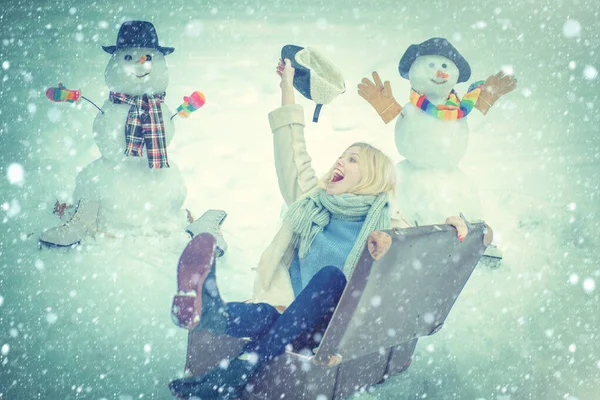 Egy lány bőrönddel. Winter World Travel - Szánkó bőrönd. Téli vakációkat tervezek. Boldog mosolygós hóembert és téli lányt a napsütéses napon. Téli hókék tónusú. — Stock Fotó