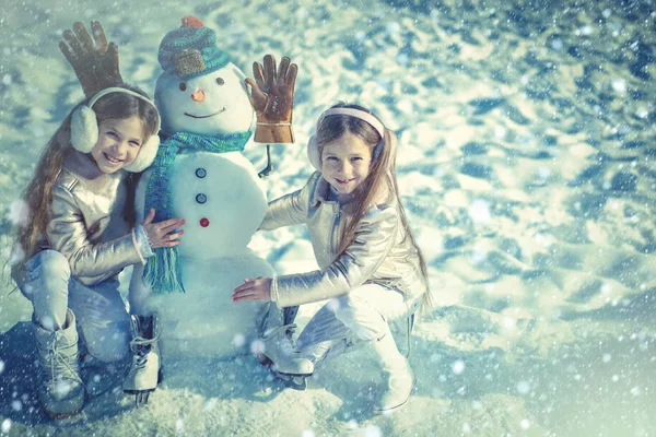 Hiver tonique bleu neige. Les enfants font bonhomme de neige sur fond de neige blanche. Enfants heureux jouant avec un bonhomme de neige lors d'une promenade hivernale enneigée . — Photo