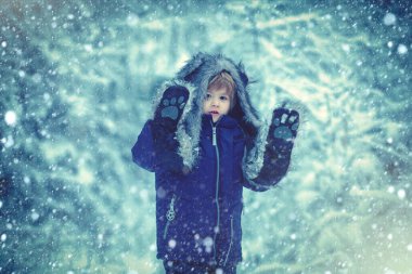 Kış parkında karla kaplı sevimli bir çocuk. Kış çocukları boş vakitlerinde. Çocukluk anıları. Çayırda güzel, karlı bir kış. Kış mavisi tonlar.
