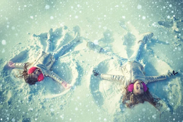 Två tjejer på en snöängelshow. Barn leker och gör en snöängel i snön. Ovanifrån. — Stockfoto