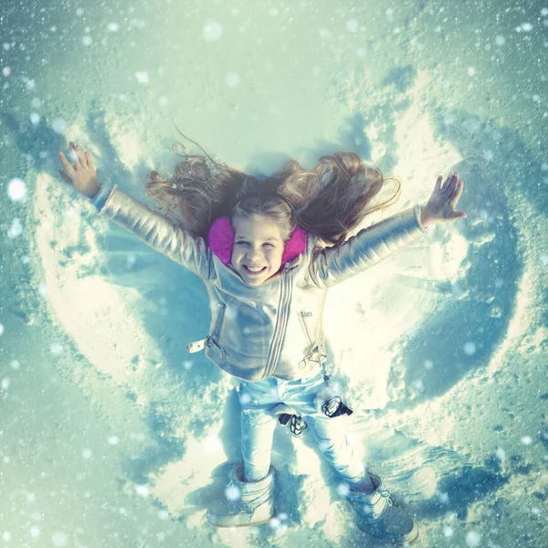 Funny kid making snow angel. Child girl playing and making a snow angel in the snow. Top view. — Stockfoto