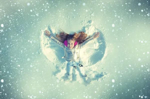 一个小孩在雪地里制造的雪天使。 笑着的孩子躺在雪地上，有着复制的空间。 有趣的孩子制造雪天使。 蓝色调. — 图库照片