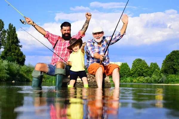 Famiglia multigenerazionale maschile. Nonno, padre e nipote pescano insieme. Padre insegna a suo figlio la pesca contro la vista del fiume e del paesaggio . — Foto Stock