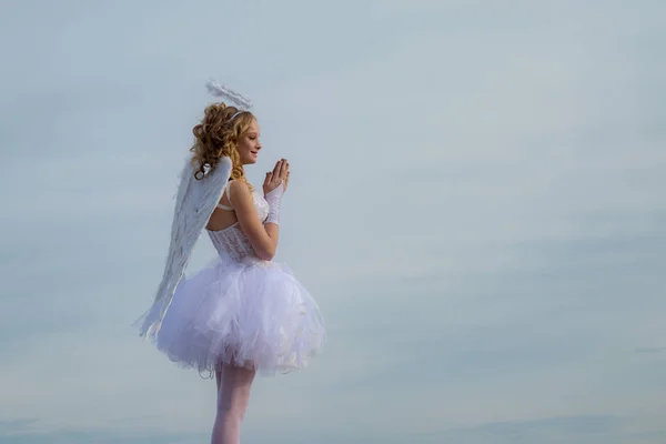 Linda niña blanca como el Cupido felicitando el día de San Valentín. Inocente chica con alas de ángel de pie con arco y flecha contra el cielo azul y nubes blancas . — Foto de Stock