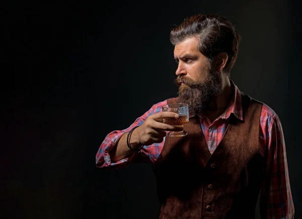 Een man met een baard heeft een glas cognac. Luxe alcoholdrankje. Vrolijke bebaarde man drinkt dure whisky.. — Stockfoto