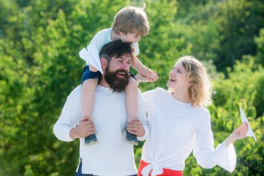 Baba, anne ve bebek dışarıda birlikte oynuyorlar. Mutlu çocuk ailesine kağıttan uçak gösteriyor. Sevgi dolu bir aile. Tatilde mutlu bir aile.