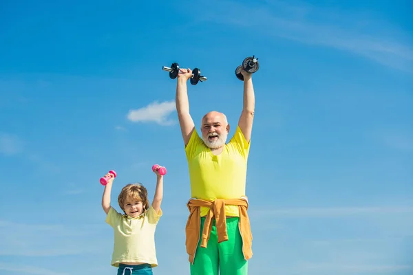Aktív egészséges élet a családnak. Idősek és gyerekek gyakorolnak a kék égen. Nagyapa és gyerek a tornateremben súlyzóznak. Egészséges életmód. — Stock Fotó