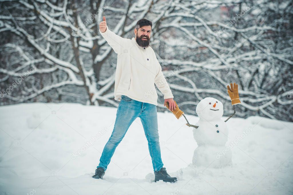 Handsome bearded man, father in winter clothes. Handsome Winter Man with snowman in frosty winter Park. Winter holidays and people concept.