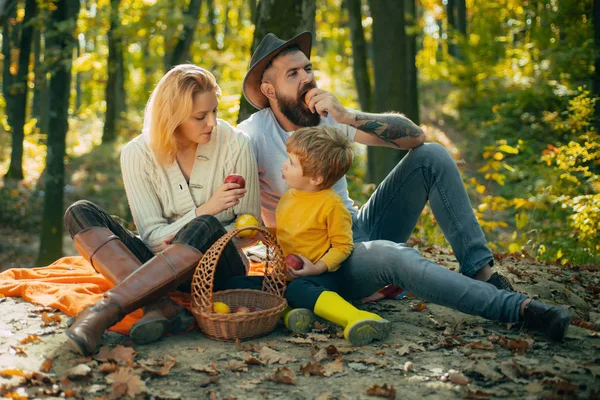 Sonbahar parkında piknik yaparken çimlerin üzerinde oturan neşeli bir aile. Güneşin ışıkları. Küçük çocuklu genç bir aile sonbahar doğasında gün batımında piknik yapıyor. Mutlu aile kokusu hariç.. — Stok fotoğraf