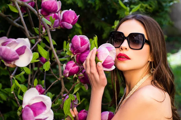 Nahaufnahme Porträt der schönen jungen brünetten Frau mit roten Lippen und gesunder Haut mit rosa Blüten in der Nähe ihres Gesichts. schöne Dame in den Blumen in Gläsern. Frühlingsblüte. — Stockfoto