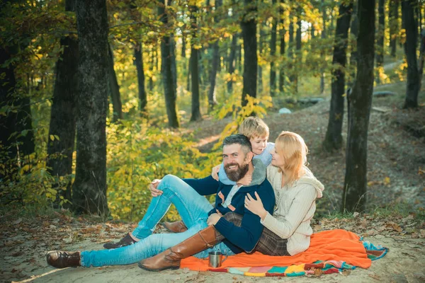 Mutlu üç kişilik aile, sonbahar güneşli altın parktaki piknik battaniyesinde oturuyor. Neşeli bir gülümseme ve herkesin mutlu bir ruh hali. Sonbahar kıyafetleri. Aile güz tatilleri. — Stok fotoğraf