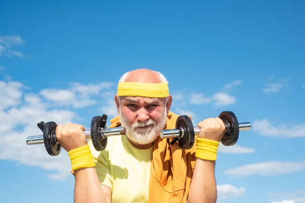 Portret van een oudere man die een halter vasthoudt. Wees in beweging. Gezondheidsclub of revalidatiecentrum voor ouderen. Senior sportman tilt halters in sportcentrum. — Stockfoto