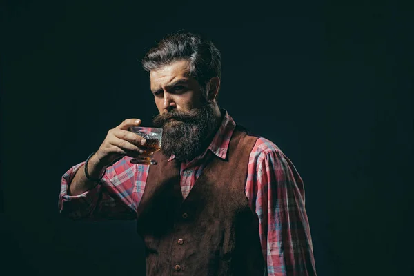 Boisson alcoolisée de luxe. Homme élégant et élégant dans l'usure classique tenant verre avec wiskey à la main. L'homme barbu joyeux boit du whisky cher. — Photo