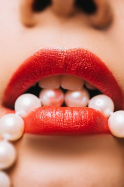 Sexy parlak kırmızı kadın dudakları inci kolye tutuyor yakın plan fotoğraf. Lüks turuncu rujlu kadın dudakları. Ağızda inci tasma tutan kadın. Yakın çekim fotoğrafı..