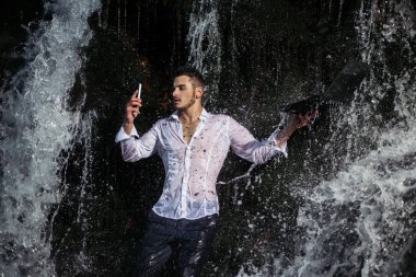 Ip68 su geçirmez korumalı yenilikçi cihazlarıyla şelalenin altında duran yakışıklı genç işadamı. Şelale arka planında alet tutan takım elbiseli çekici bir adam..