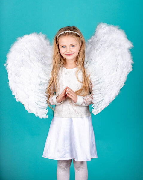 Cute child girl in white dress standing over color background. Child angel with a beautiful wings. Happy little Angel. Mischievous little angel girl standing with your clenched fists.