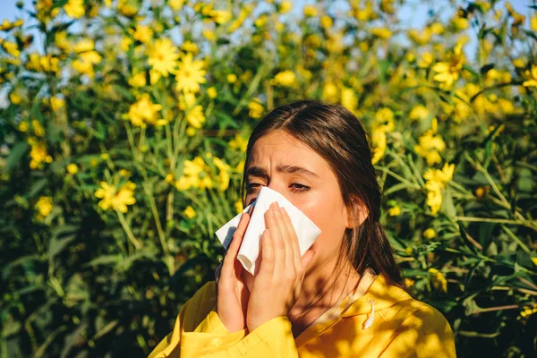 Nő szalvétával harcol virágallergiával a szabadban. Allergia a virágzásra. A fiatal nő tüsszenteni fog. Tüsszentés és orrfolyás a pollentől. Allergia orvosi szezonális virágok koncepció. — Stock Fotó