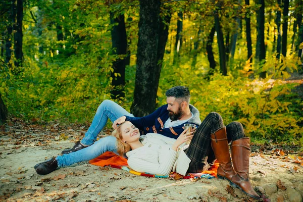 Autumn season concept. Young happy family having good time and smiling at autumn colorful park. Bearded man playing with blond hair of his wife. Sensual romantic photo.