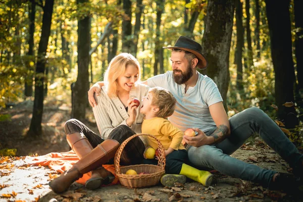 Korg med picknick måltid och leksaker för barnet. Lycklig familj på tre som ligger i gräset på hösten. Begreppet lycklig familj. Unga leende familj gör en picknick på en höstdag. — Stockfoto