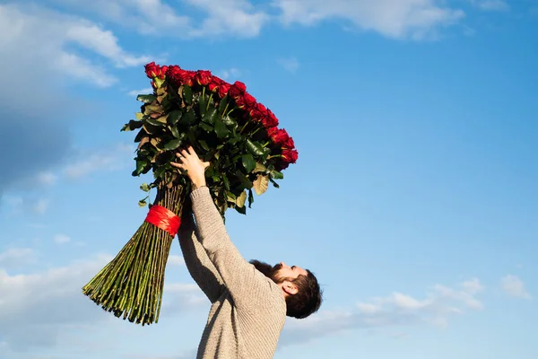 Happy Saint Valentines Day. Handsome man giving flowers to his lover on Valentines Day. Man holding chic bouquet of red roses.