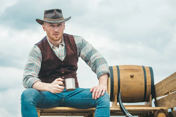 Hombre macho barbudo guapo. Hombres estándar de belleza. Ejemplo de verdadera masculinidad. Vaquero con sombrero. La vida occidental. Chico sin afeitar con sombrero de vaquero y camisa trenzada bebiendo alcohol . —  Fotos de Stock