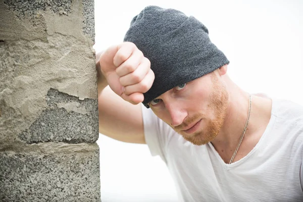 Sexy ginger unshaven brutal man wearing beanie cap standing near the wall. Man style and fashion. Brutal masculine man close up studio portrait. Handsome man with ginger red hair. — Stock Photo, Image