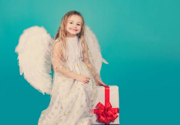 Valentijnsdag. Engelenkind uit de hemel geeft je een geschenk. Gezicht van mooie kleine engel meisje op kleur achtergrond. Een engeltje met prachtige vleugels. Ziet eruit als een engel.. — Stockfoto