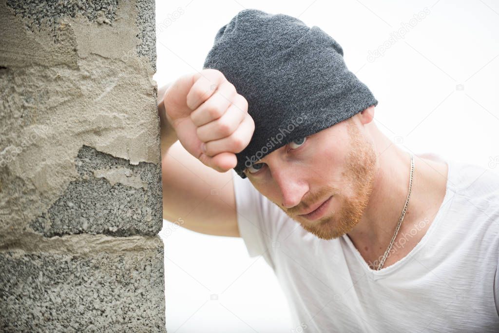 Sexy ginger unshaven brutal man wearing beanie cap standing near the wall. Man style and fashion. Brutal masculine man close up studio portrait. Handsome man with ginger red hair.