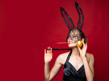 Paskalya bayramını kutlayan maskeli ve kulaklı seksi Paskalya tavşanı. Kırmızı arka planda izole edilmiş tavşan kostümlü tahrik edici genç bir kadın. Seksi tavşan konsepti.