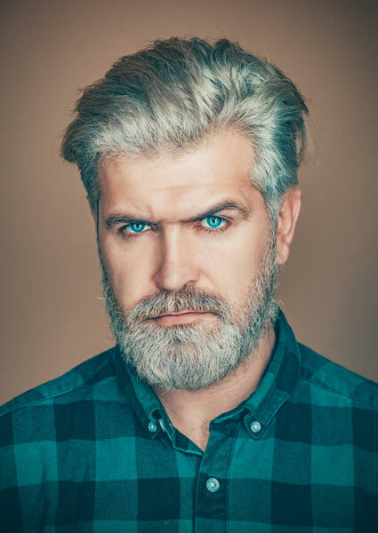 Isolated shot of young handsome male with beard mustache and trendy hairdo. Portrait of satisfied businessman against grey wall.