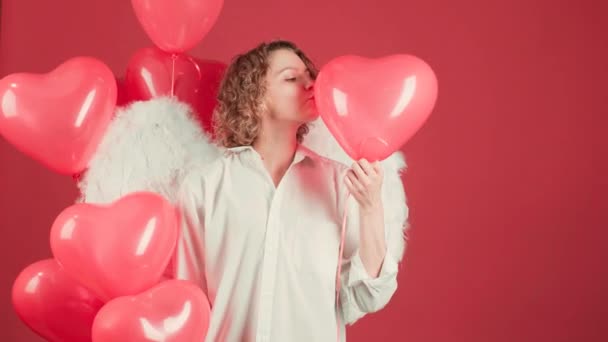 Beauty fashion model angel girl with Valentine Heart in her hands. Funny angel girl with beautiful surprised face and heart balloon. On red background isolated. — Stock Video