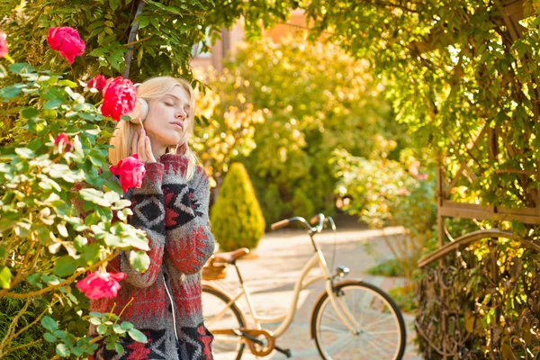 Feliz joven en el parque en el soleado día de otoño. Chica hermosa alegre en suéter gris, auriculares y bicicleta al aire libre en hermoso día de otoño. Naturaleza de caída y concepto de personas . —  Fotos de Stock