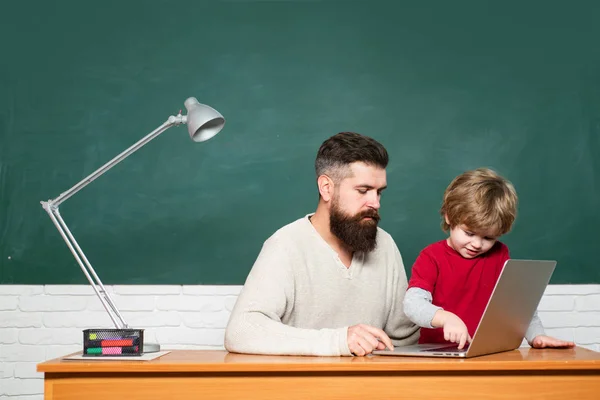 Nauczyciel i uczeń szkoły podstawowej w klasie. Nauczyciel i uczeń korzystający z laptopa w klasie. Przestrzeń do kopiowania tablic. Ojciec i syn. Dzieciak ze szkoły podstawowej i nauczyciel w klasie w szkole. — Zdjęcie stockowe