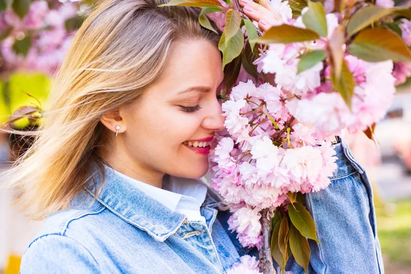 Donna bionda con albero Sakura in fiore e giornata di sole. Fiori primaverili con sfondo blu e nuvole . — Foto Stock