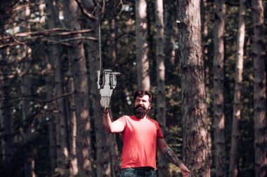 Ormanda testere ile kereste işçisi. Oduncu gibi poz veren şık bir genç adam. Oduncu işçi ormanda elektrikli testereyle dikiliyor. Tahta testereyi tutan oduncu.