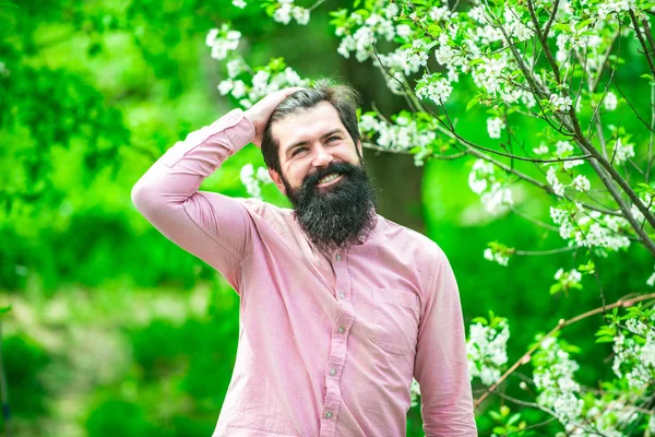 Retrato de fazendeiro barbudo. Um homem bonito passa algum tempo no pomar das flores. Retrato de homem barbudo contra flor campo de mola verde . — Fotografia de Stock