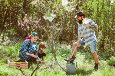 Mutlu aile bahar bahçesi geçmişi üzerinde çalışıyor. Çevre hayatı. Doğada eğlenen çocuklu genç bir aile.