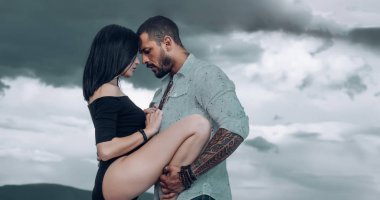 Duygusal bir kadın dramatik gri arka planda vahşi bir adama bacağını kaldırıyor. Gökyüzüne karşı güzel bir çift. Çiftler dışarıda romantik bir yürüyüş yapar. Gerçek aşk konsepti.