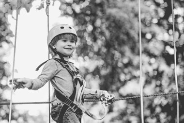 Cargo net climbing and hanging log. Cute school child boy enjoying a sunny day in a climbing adventure activity park. Toddler kindergarten.