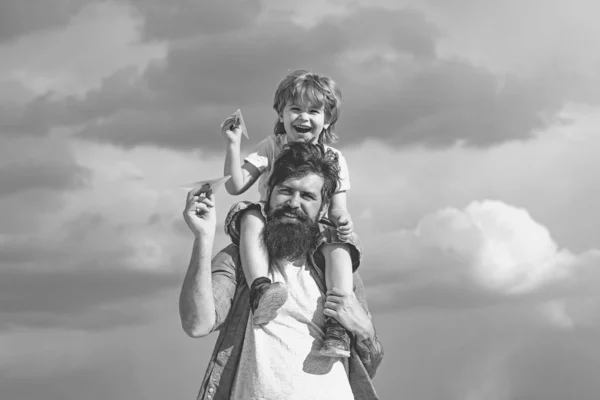 Generation. Vater gibt Sohn im Park zurück Vater und Sohn bauen gemeinsam ein Papierflugzeug. Porträt eines glücklichen Vaters, der seinem Sohn Huckepack auf den Schultern gibt und aufblickt. — Stockfoto