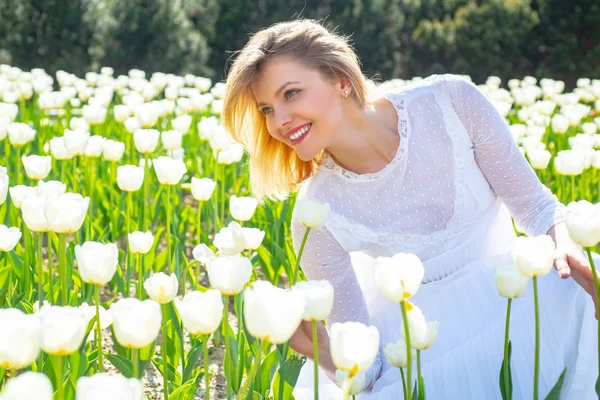 Jarní módní koncept. Žena v poli bílých tulipánů se usmívá. Životní styl ženy pocit dobré relaxace a šťastnou svobodu na přírodní tulipán farmě. — Stock fotografie