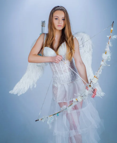 Schattige kleine vrouwelijke cupido schiet een strik. Angel kinderen meisje met witte vleugels. onschuldig meisje met engel vleugels staan met pijl en boog tegen witte achtergrond geïsoleerd. Onschuldig meisje. — Stockfoto