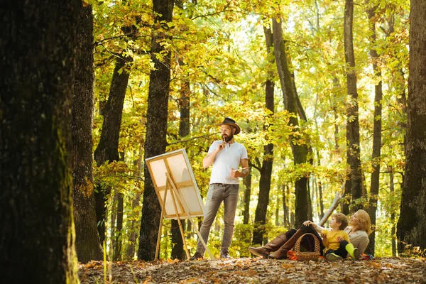 Start new picture. Portrait of young bearded smiling middle age white man artist drawing in open plein air outside with watercolor on paper at easel. Family picnic at autumn nature. — 스톡 사진