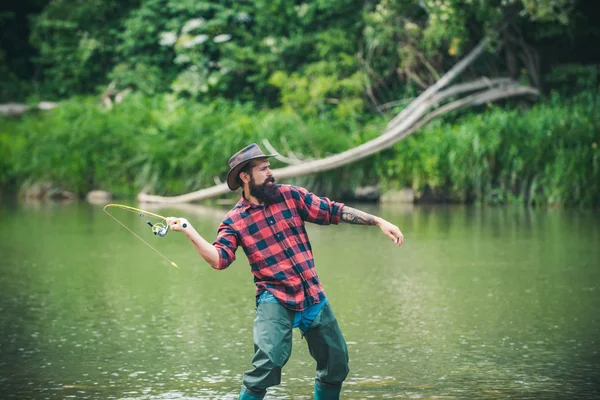 Un bel pescatore col cappello. La pesca richiede di essere consapevoli e pienamente presenti nel momento. Allegro pescatore che pesca in un fiume all'aperto. Pesca d'acqua dolce lago stagno fiume . — Foto Stock