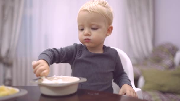 Food and Drink - Child eat concept. Little boy having breakfast in the kitchen. Happy baby boy spoon eats itself. — Stock Video